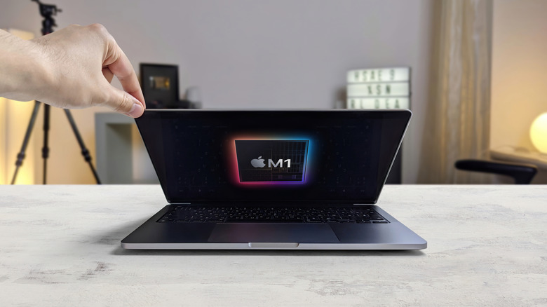 Person opening a MacBook with an Apple M1 chip graphic displayed on the screen.