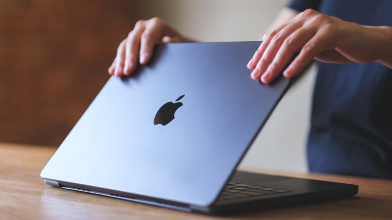 Close-up of a person opening a silver MacBook on a desk.